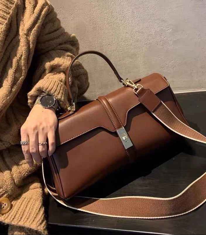 Brown leather handbag held by a person wearing a brown sweater.