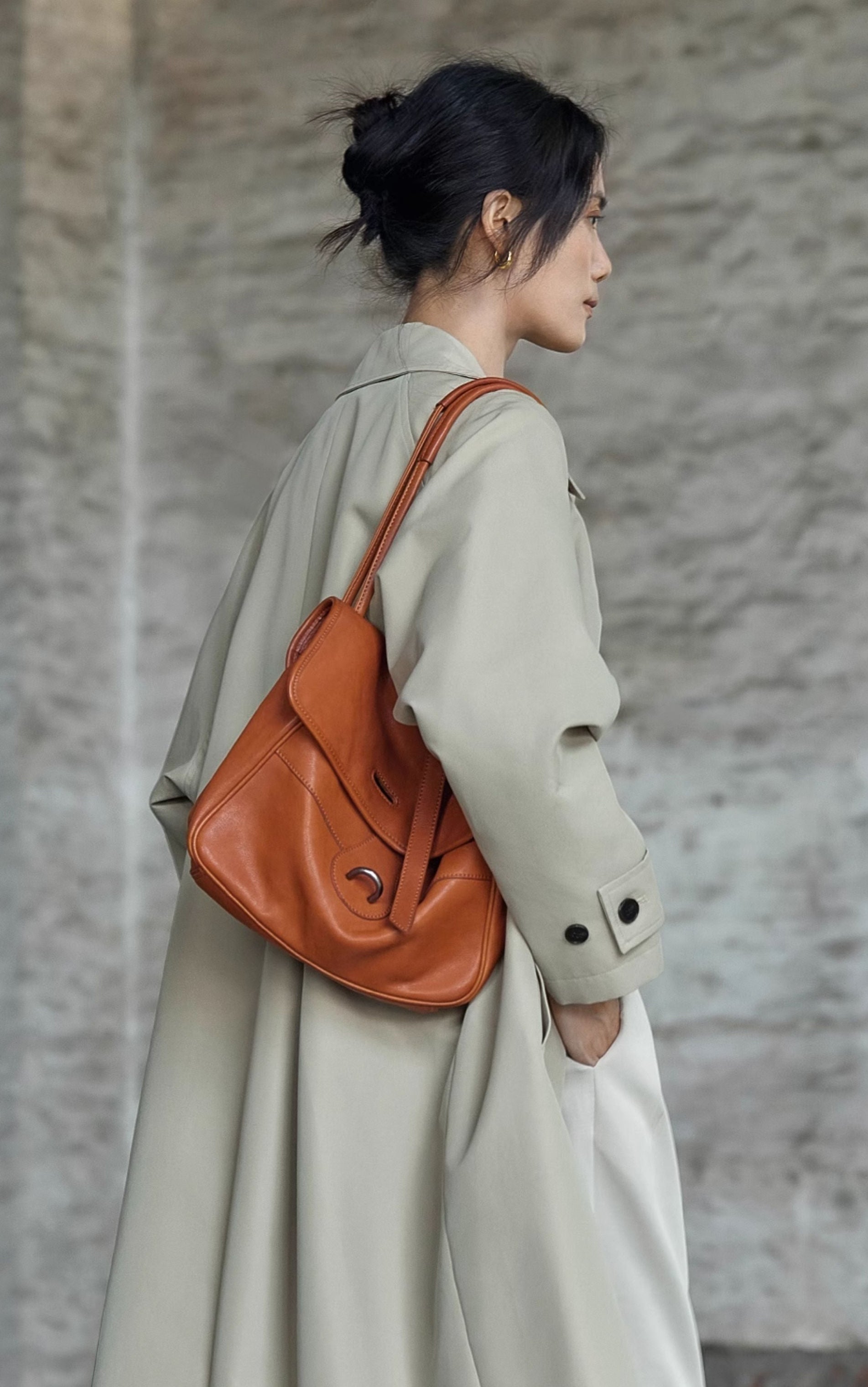 Person wearing a beige coat with an orange leather bag against a textured wall.