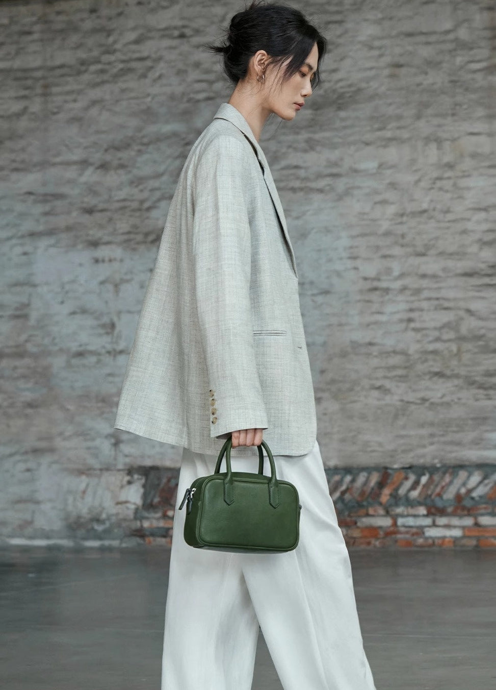 Woman holding a green handbag against a textured wall.