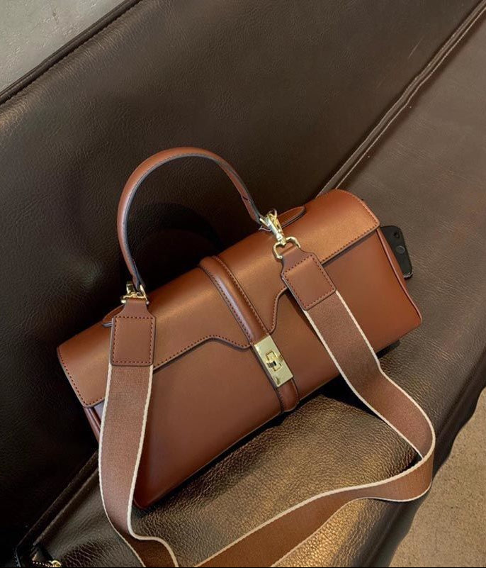 Brown leather handbag with a strap on a brown textured surface